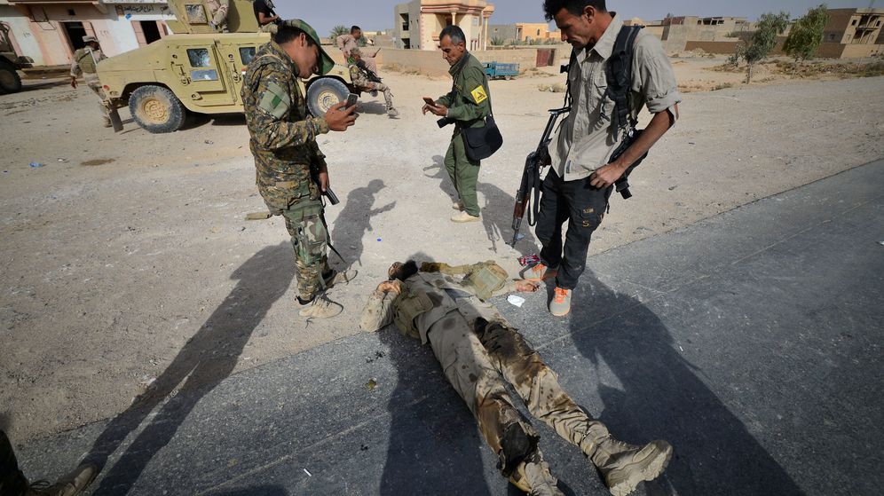 Foto: Miembros de una milicia chií observan el cadáver de un militante del ISIS tras la liberación de la ciudad de Al Qaim, en noviembre de 2017. (Reuters)