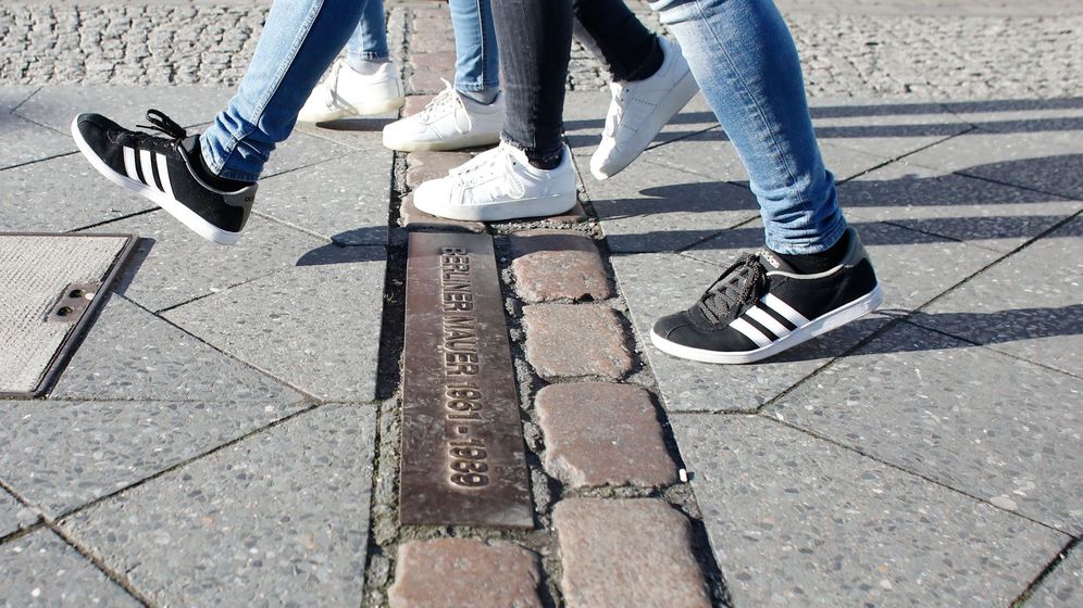 Foto: Varias personas caminan sobre los adoquines que marcan la antigua división del Muro de Berlín. (EFE)